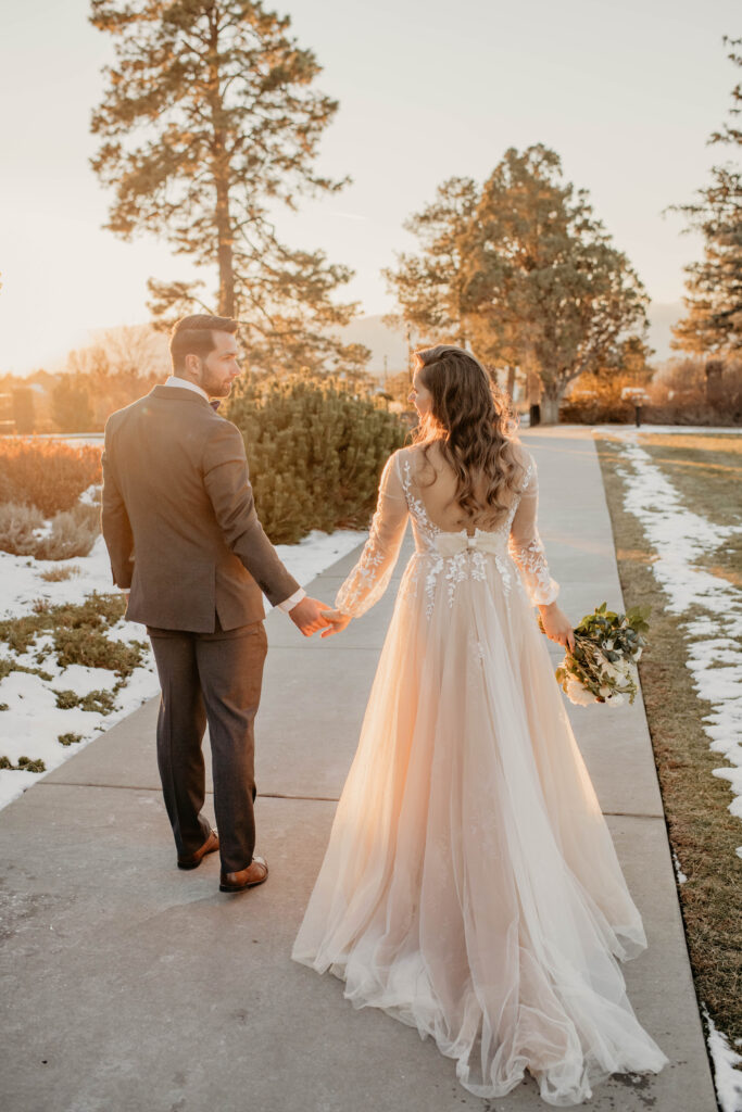 Bride and groom walking down snowy path during golden hour.