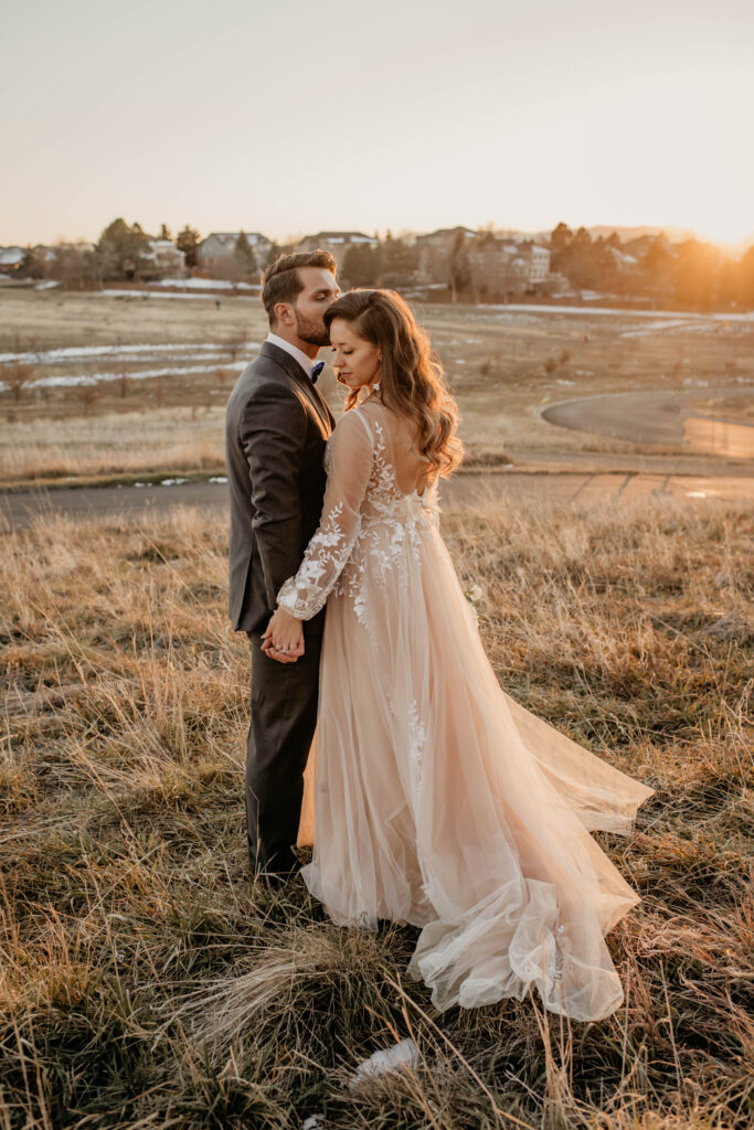 Bride and groom standing in snowy field during golden hour.