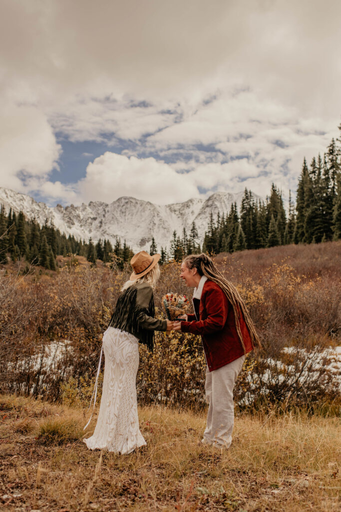 Couple saying vows in front of snowy mountain range.
