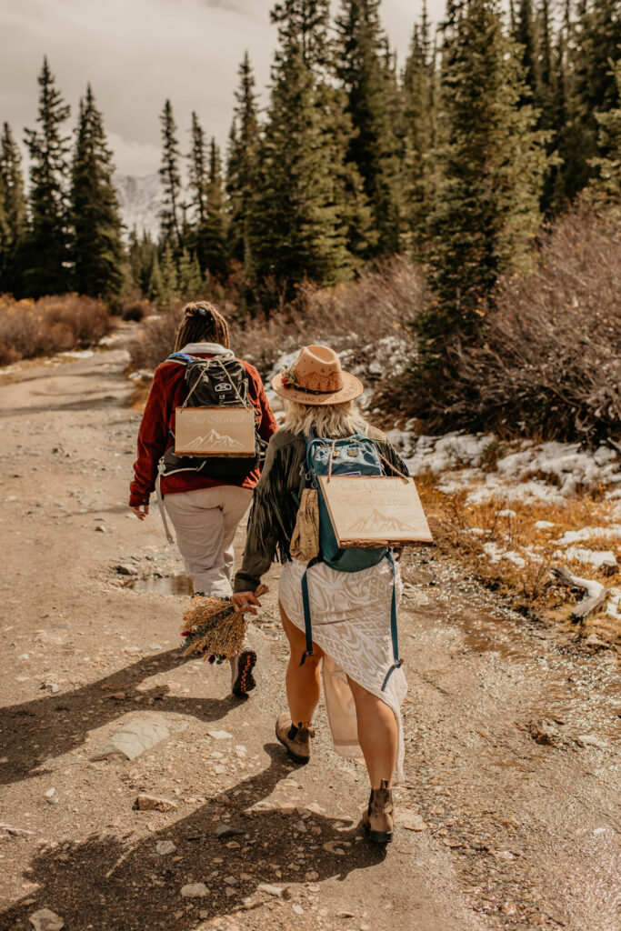 Eloping couple hiking in wedding attire with packs and "just married" signs.
