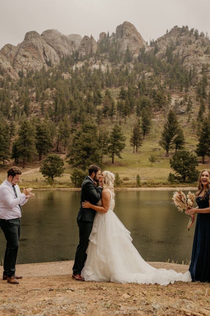 Wedding couple sharing first kiss at lake's edge inside RMNP.