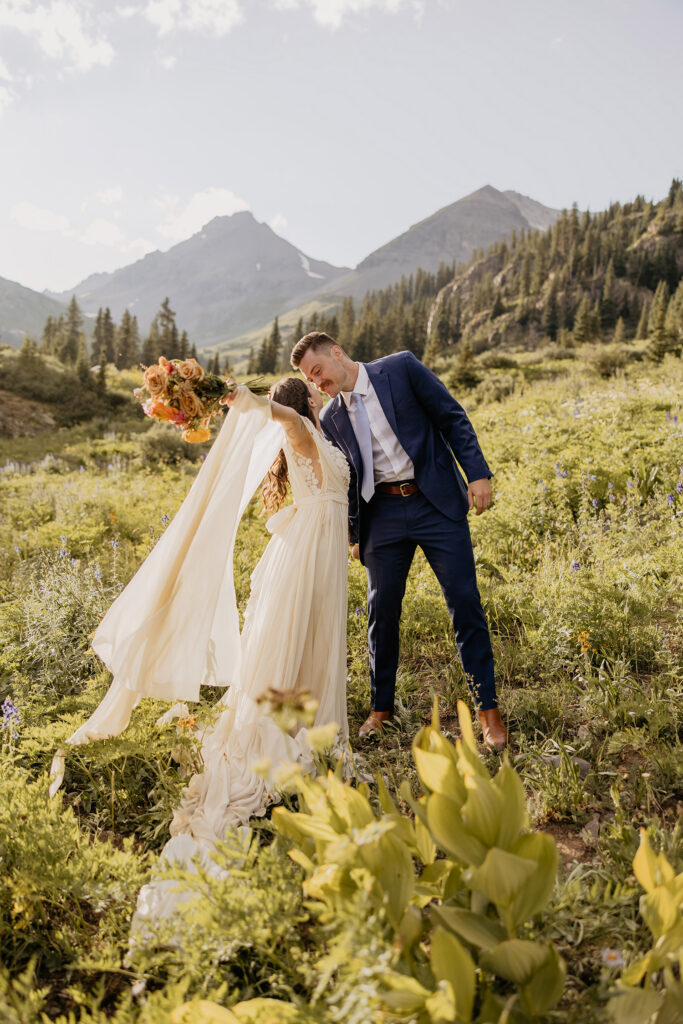 Bride, wearing flowy elopement wedding dress, and groom kissing in field of wildflowers