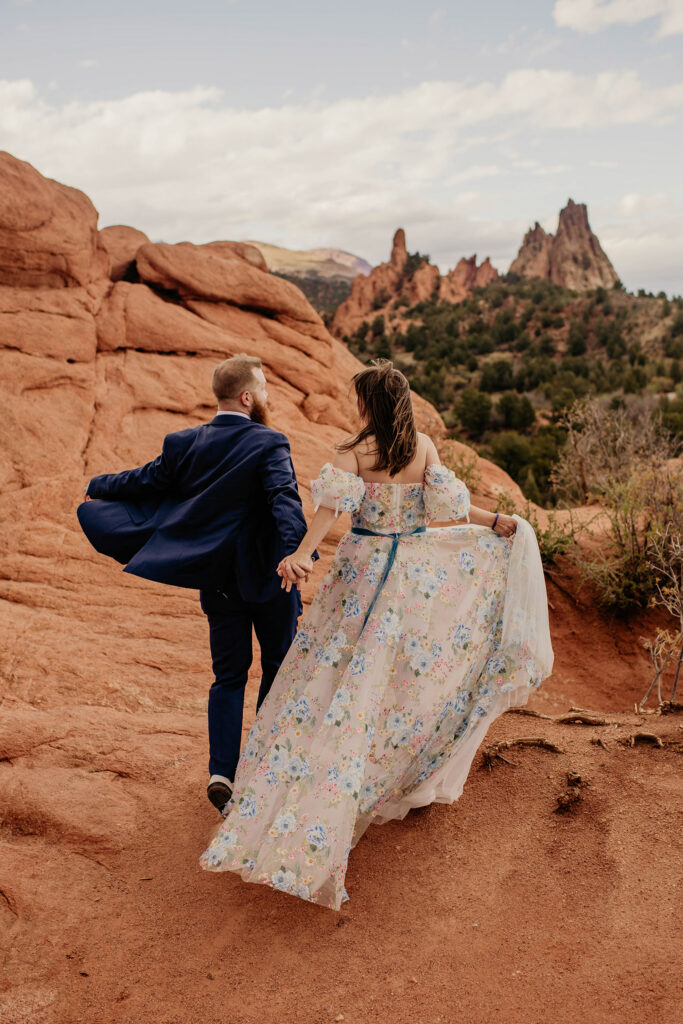 Couple exploring red rocks of Garden of the Gods. Bride is wearing embroidered elopement wedding dress.