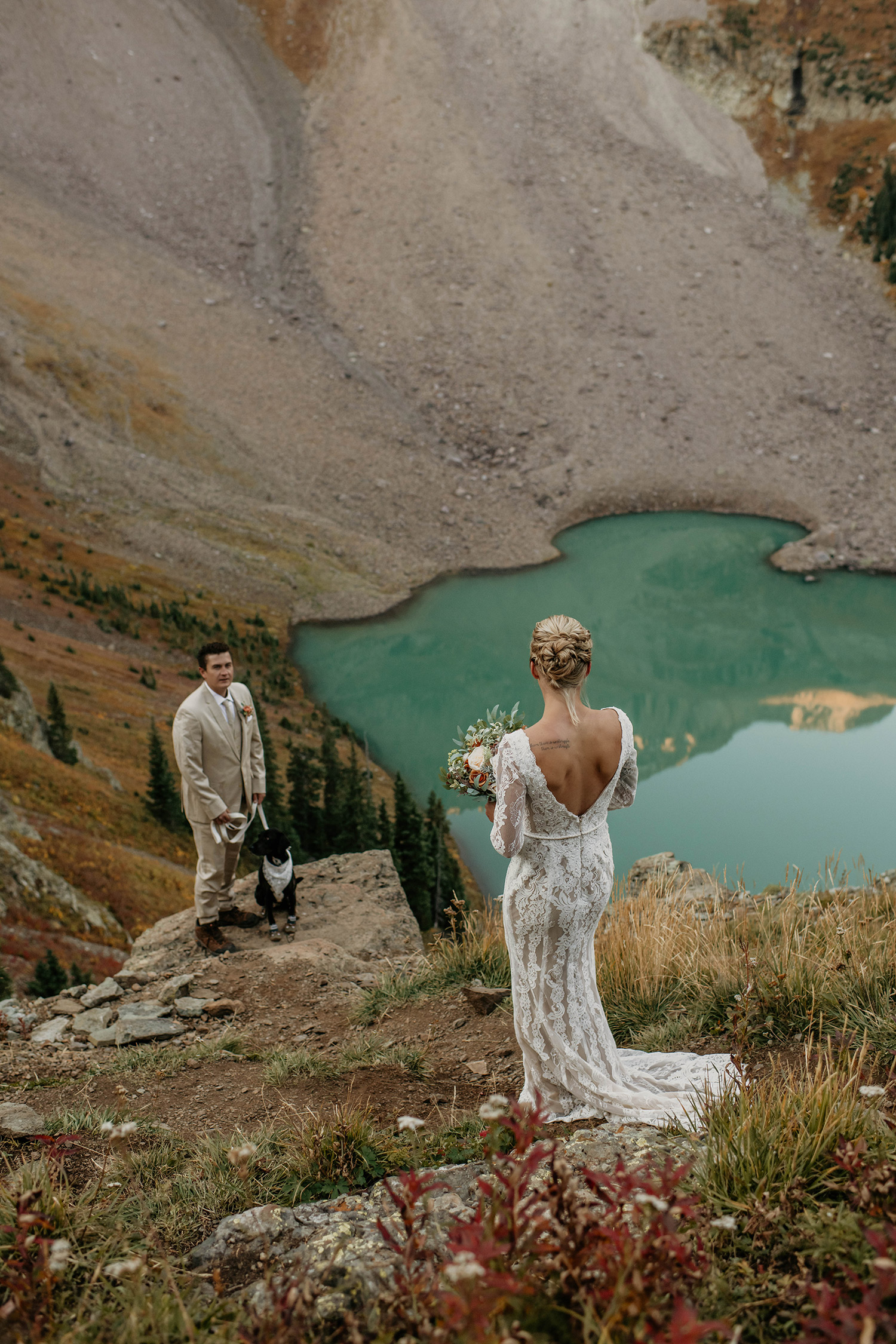 Bride walking toward groom above alpine lake in Ridgway, Colorado.