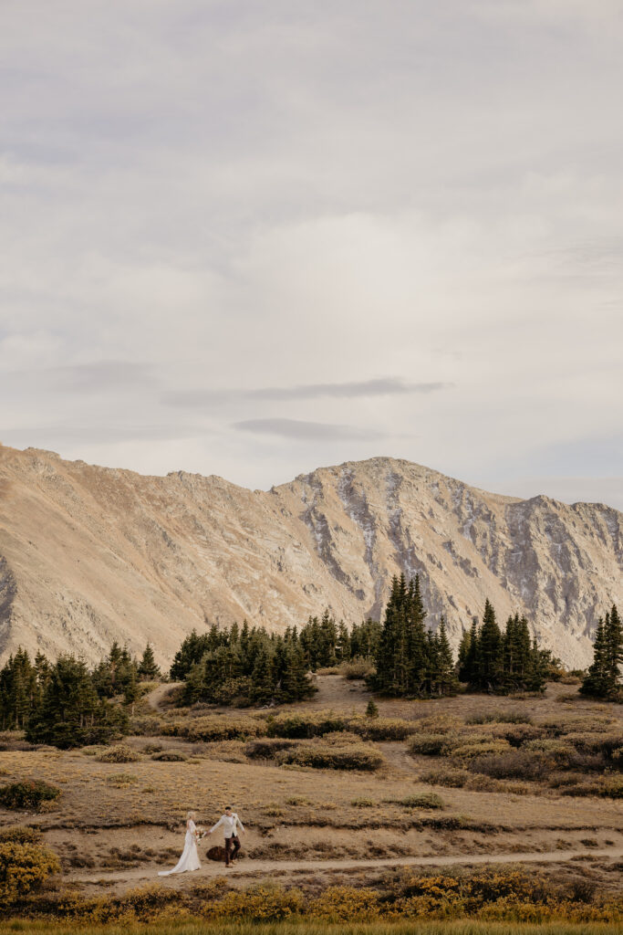 Wedding couple walks together in front of panoramic mountain views.