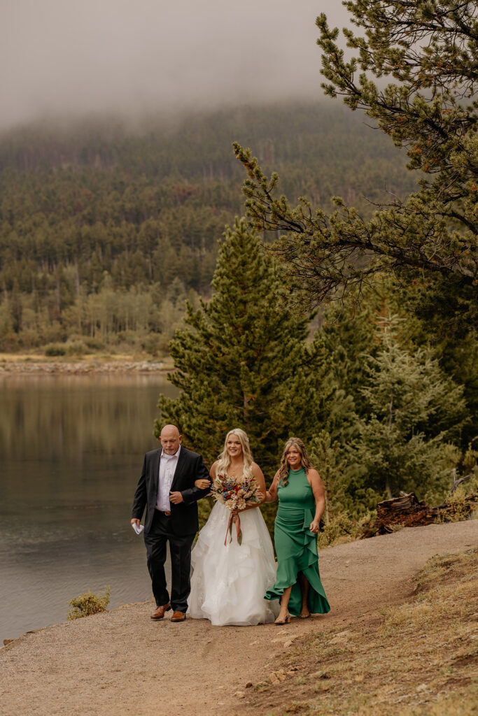 Bride walking with parents down path during elopement at Lily Lake.