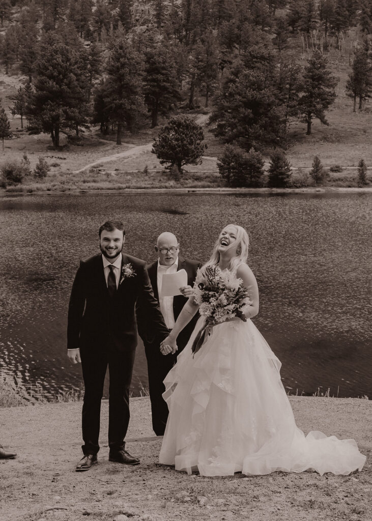Wedding couple laughing towards their guests with alpine lake in background.