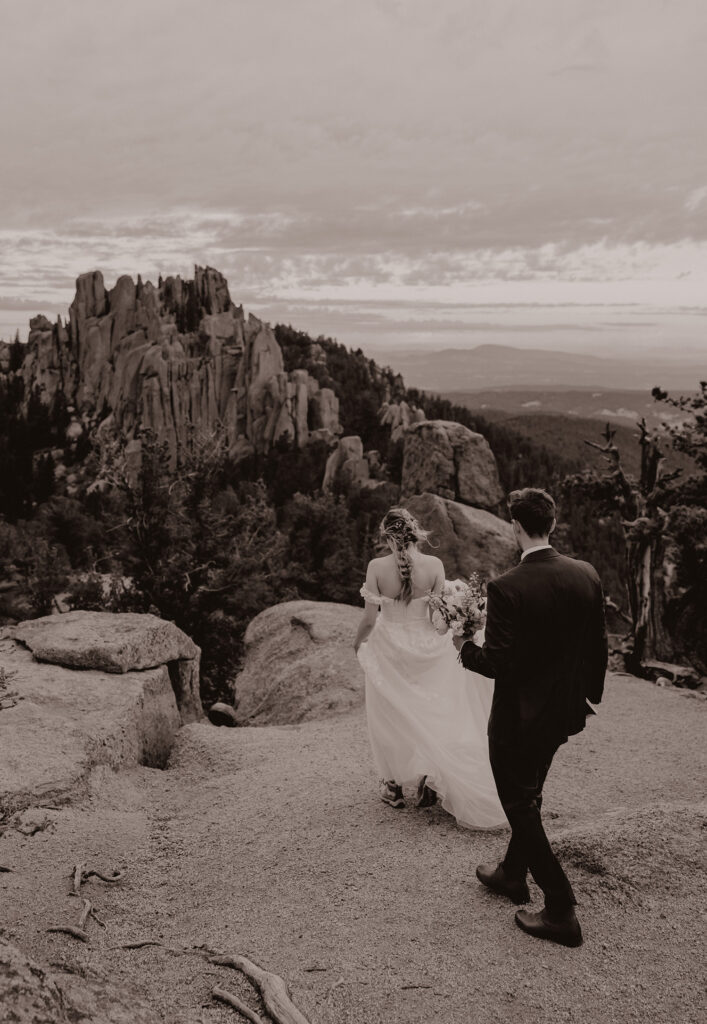 Wedding couple walking towards elopement ceremony spot in front of granite spires.