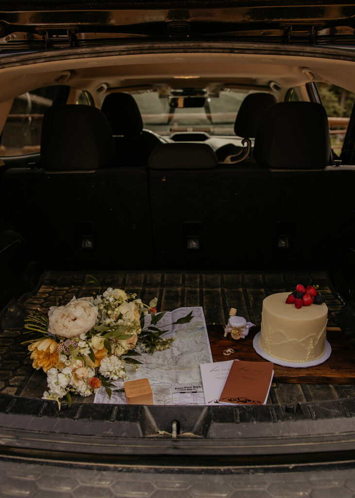 Elopement details - bouquet, map, vow books, rings and cake - laid out in back of subaru. 