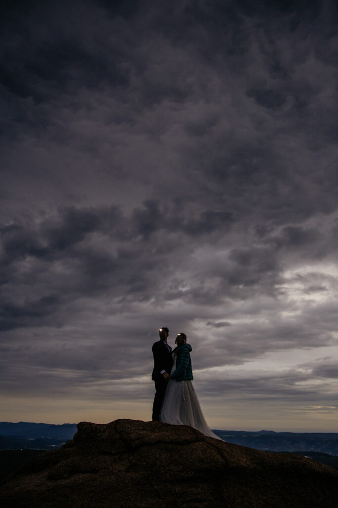 Wedding couple standing together on rock with headlamps on before the sun rises.