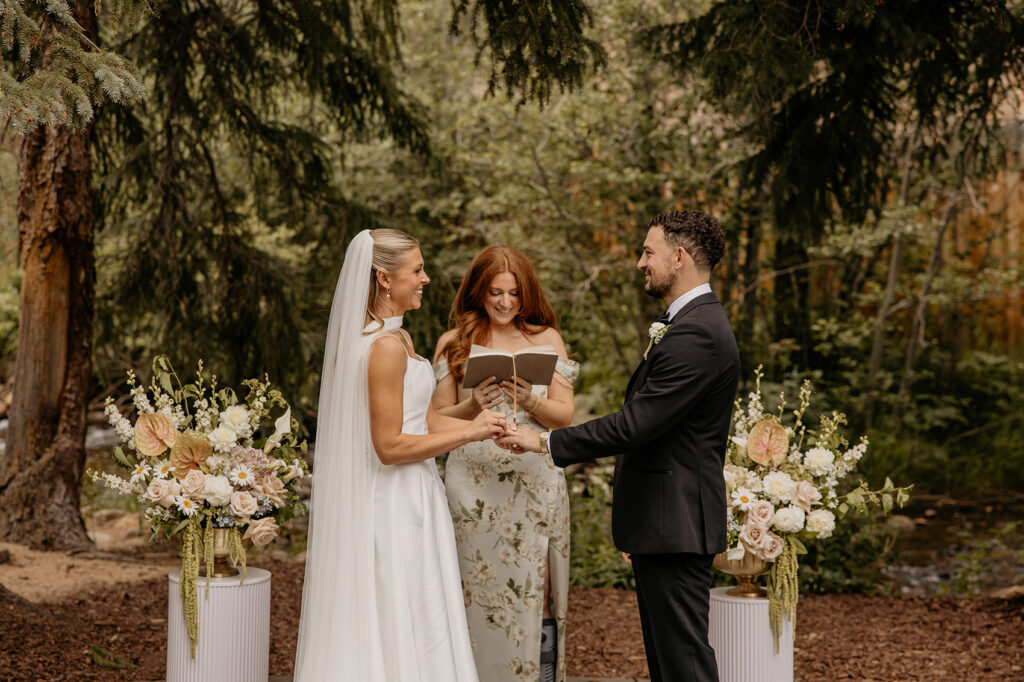 Couple exchanging vows and rings at the ceremony site by the creek at Blackstone Rivers Ranch.