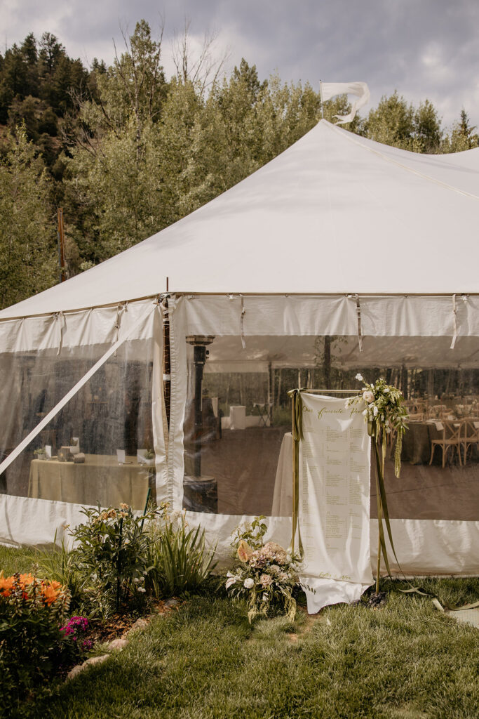 Cloth seating chart flowing in the wind outside of sailcloth tented wedding.