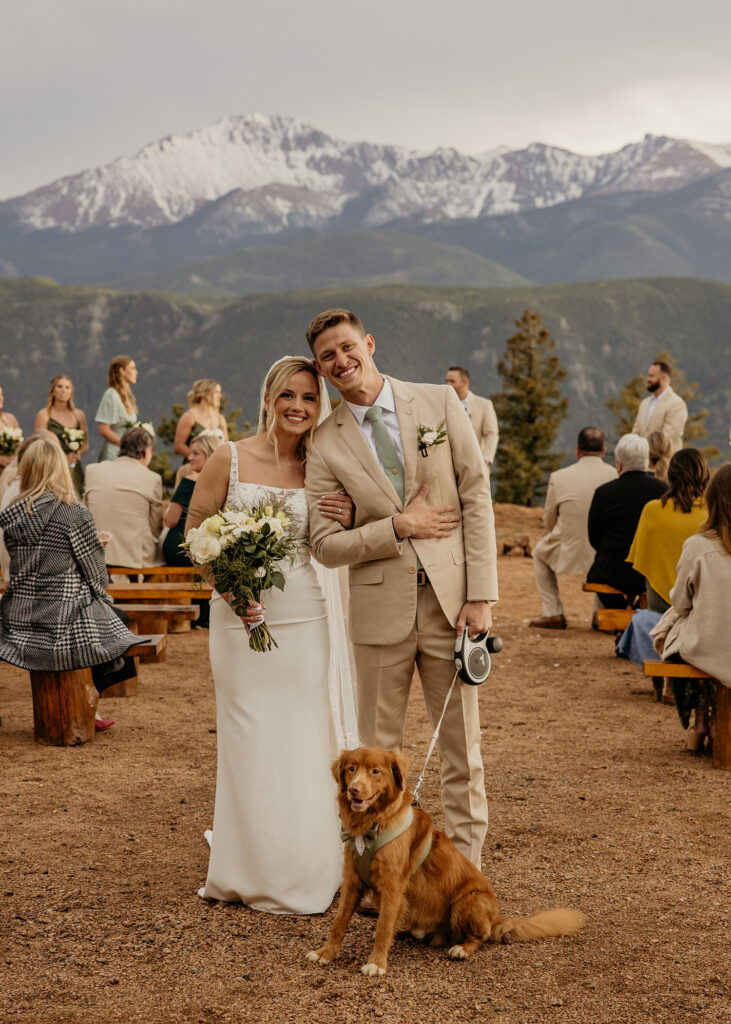 Bride and groom pose with dog after walking down the aisle.