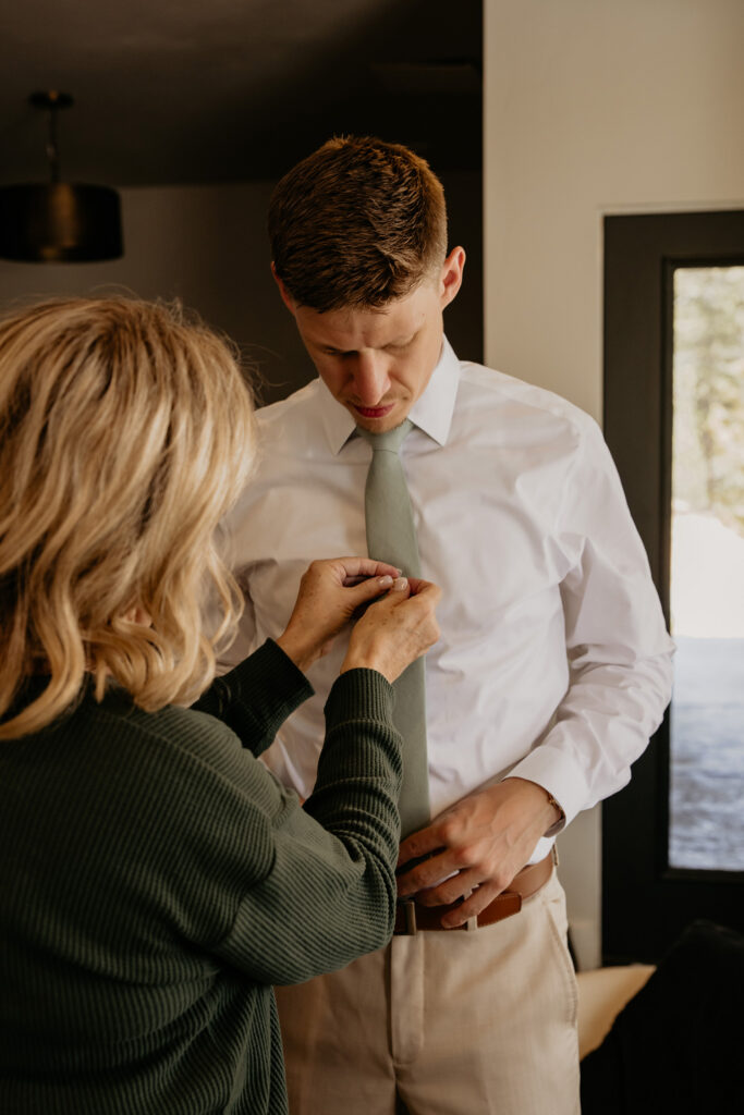 Mother of the groom helps groom with tie pin. 